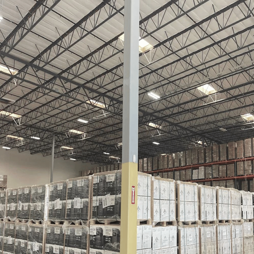 A large industrial warehouse room with metal beams from floor to ceiling. The room is full of stacked boxes and organized product